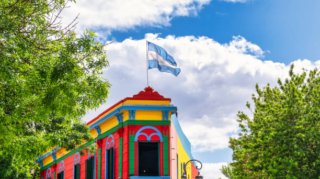 Typical brightly colored building on Caminito street in La Boca district, Buenos Aires, Argentina - Argentine flag on top of building with blue sky with clouds